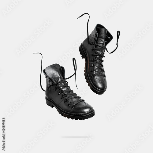 Black flying leather men's or women's boots isolated on light gray background. Fashionable stylish hiker boots. Creative minimalistic shoes background. Rough unisex boots. Layout with footwear Mock up