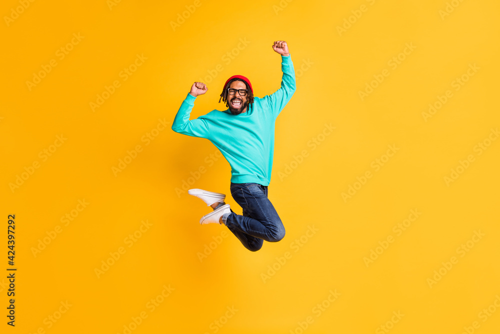 Full size profile photo of brunette optimistic guy jump wear cap spectacles pullover jeans isolated on yellow color background