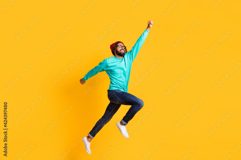 Full body profile side photo of young african man happy positive smile jump up superhero isolated over yellow color background Full body profile side photo of young african man happy positive smile jump up superhero isolated over yellow color background