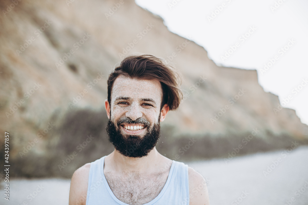 portrait of a stylish young man with a beard and a face on which the sea sand on the background of the sea shore portrait of a stylish young man with a beard and a face on which the sea sand on the background of the sea shore