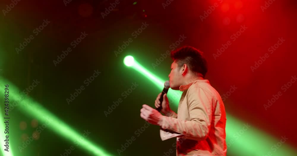 Asian vocal rock star band musician performing in stage in night club with spotlight and colorful laser ray. Singer playing to the crowd audience on music festival indoor concert Asian vocal rock star band musician performing in stage in night club with spotlight and colorful laser ray. Singer playing to the crowd audience on music festival indoor concert