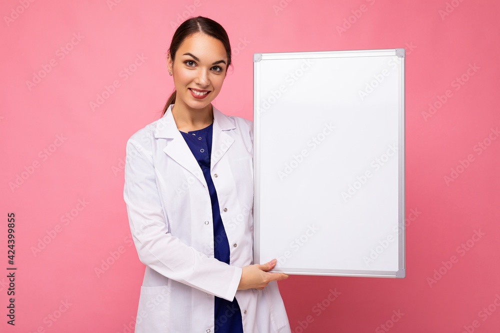 Young of beautiful happy brunet woman wearing medical white coat holding white magnetic board for mockup isolated on pink background with empty space Young of beautiful happy brunet woman wearing medical white coat holding white magnetic board for mockup isolated on pink background with empty space