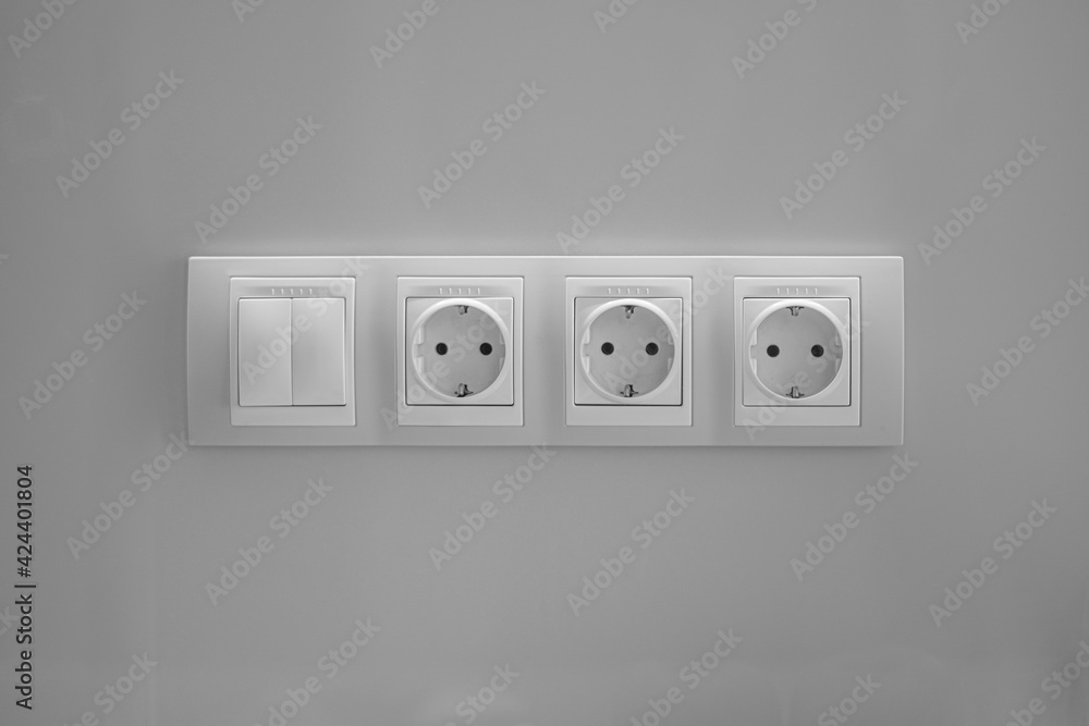Three plastic sockets with a double switch on a gray wall. Textured. Three plastic sockets with a double switch on a gray wall. Textured.