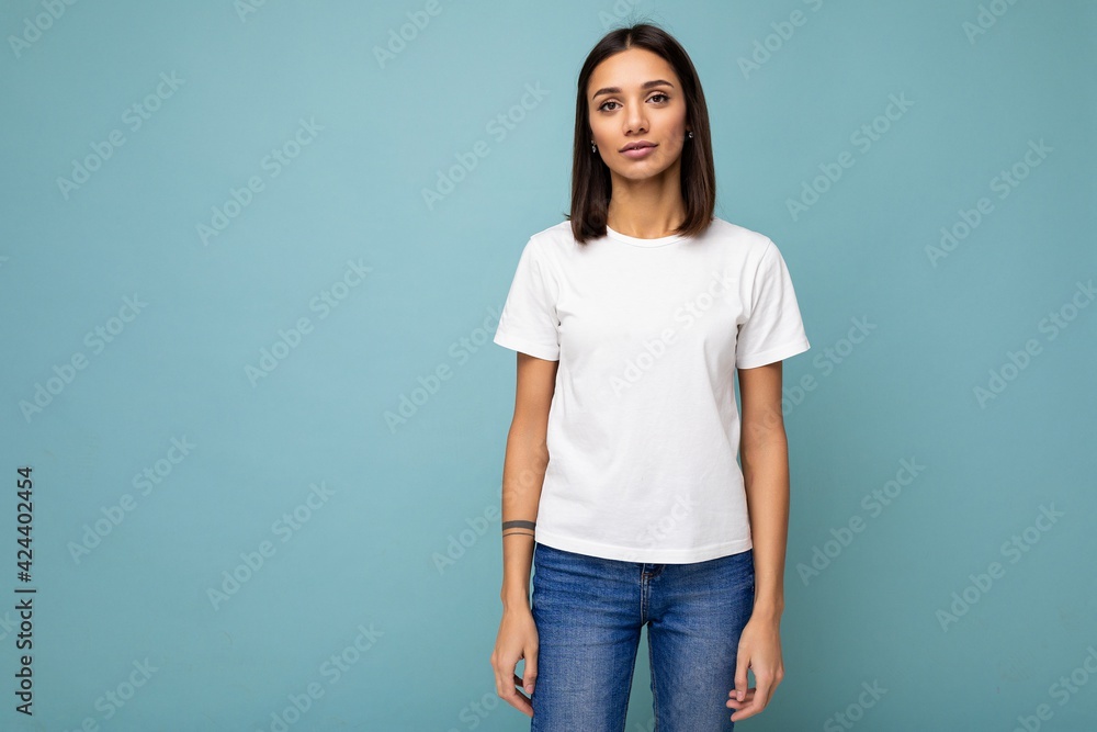 Portrait of young beautiful brunette woman wearing trendy white t-shirt with empty space for mock up. Sexy carefree female person posing isolated near blue wall in studio with free space. Positive Portrait of young beautiful brunette woman wearing trendy white t-shirt with empty space for mock up. Sexy carefree female person posing isolated near blue wall in studio with free space. Positive
