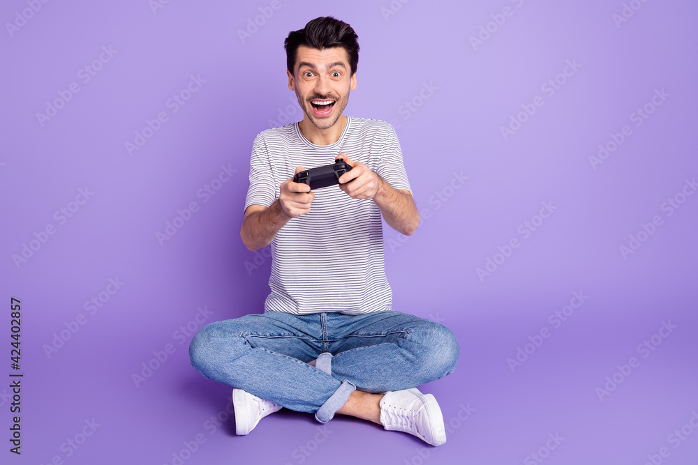 Photo of guy hold joystick open mouth play game have fun wear white t-shirt jeans footwear isolated violet background Photo of guy hold joystick open mouth play game have fun wear white t-shirt jeans footwear isolated violet background