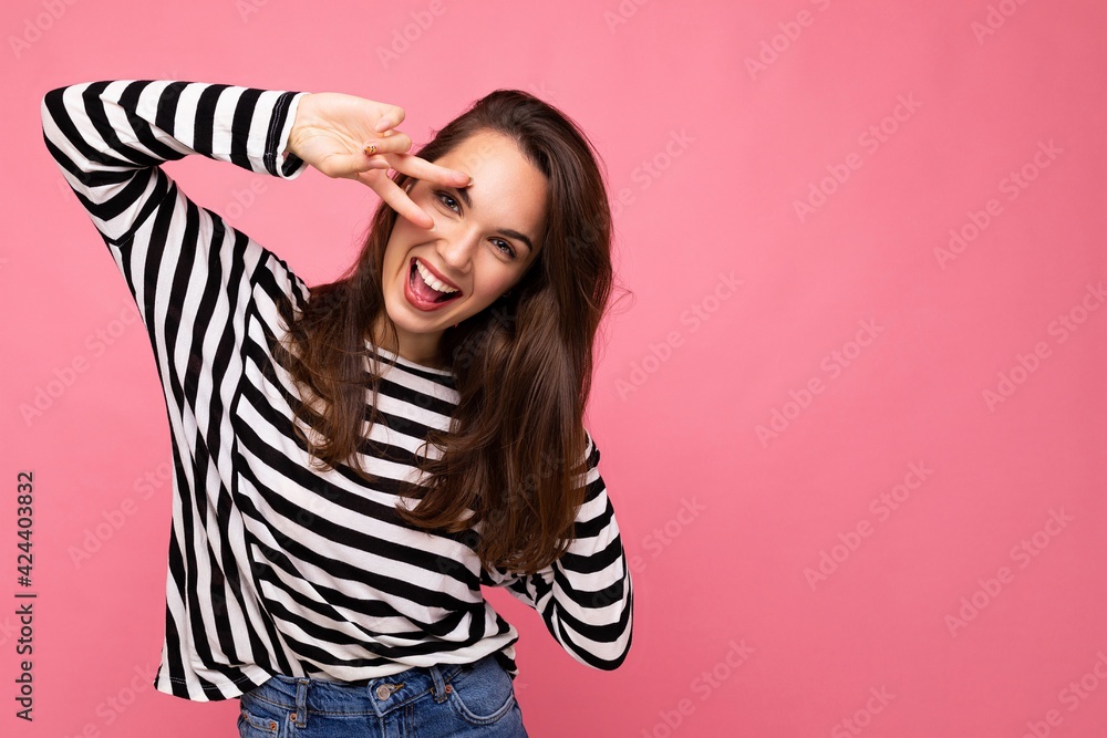 Fototapeta premium Shot of young european positive smiling winsome happy beautiful brunette woman with sincere emotions wearing casual striped pullover isolated on pink background with copy space