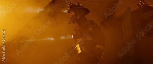 Slika na platnu Dramatic silhouette of American firefighter in full gear exploring the huge fire