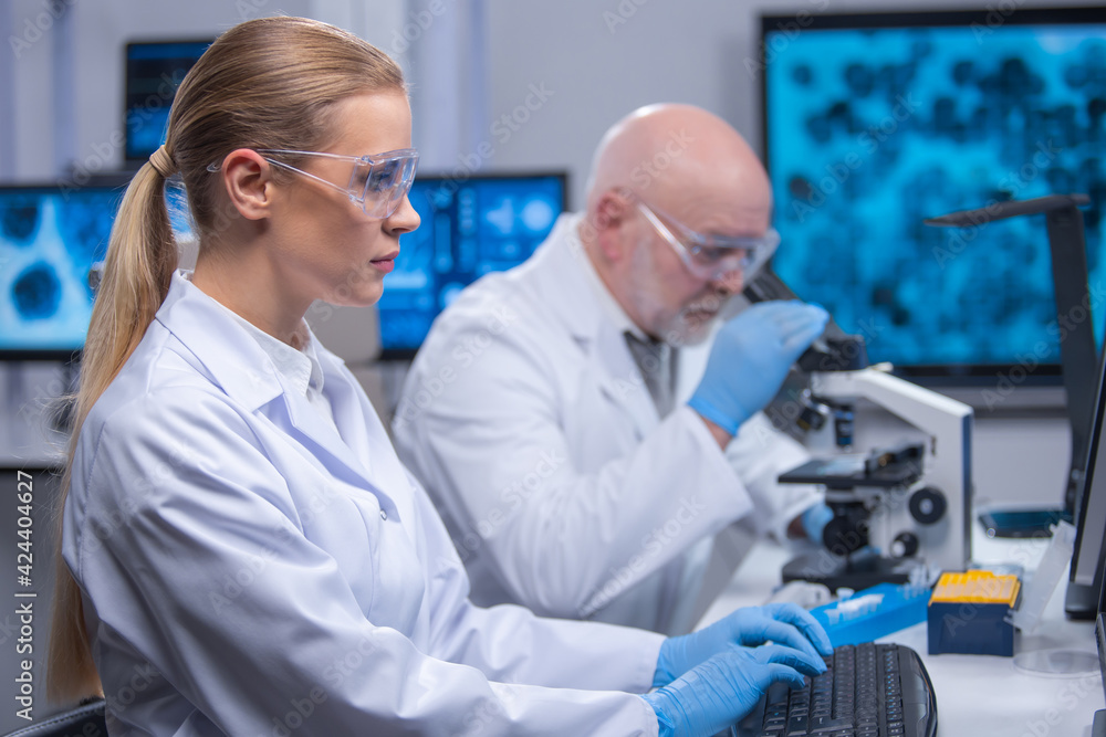 Professor and his young and professional laboratory assistant are doing scientific experiment in a modern laboratory. Genetic engineers workplace. The concept of science, medicine and vaccine. Professor and his young and professional laboratory assistant are doing scientific experiment in a modern laboratory. Genetic engineers workplace. The concept of science, medicine and vaccine.