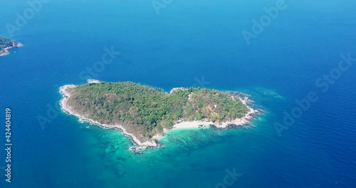 Aerial: forest of palm trees on a tropical island with bright white sand beach. In the bright and dark turquoise sea. from left to right wide angle.