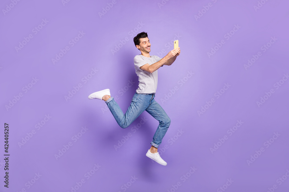 Photo of guy jump hold telephone texting wear white t-shirt jeans footwear isolated purple background