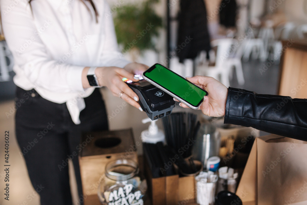 Closeup of female paying with smartphone during Covid-19 pandemic. Cashier hand holding credit card reader machine while client holding phone for NFC payment. Green screen. Mock up