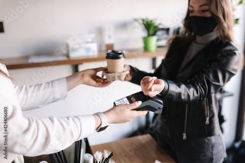Woman with face mask serving in coffee shop open after lockdown. Woman pay using smarphone and nfc technology. Closeup of human hands, making by means of contactless payment