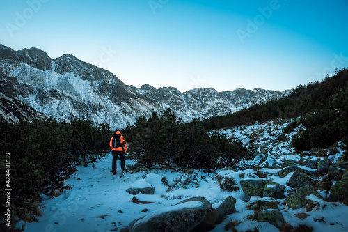 Early morning in High Tatra Mountain valley, Poland. Lonely tourist in an orange jacket hiking on a trail to the peaks. Selective focus on the ridge, blurred background.