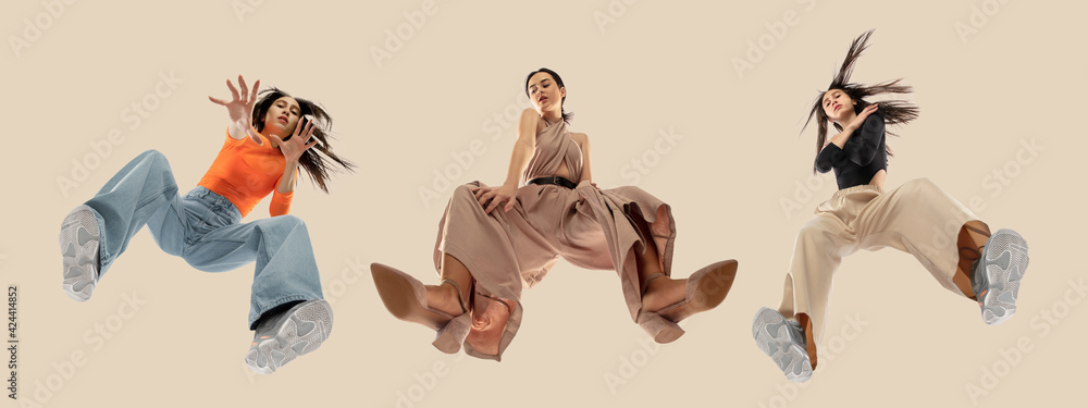 Young stylish women in modern street style outfit isolated on brown background, view from the bottom. Fashionable models, musicians, rappers performing. - obrazy, fototapety, plakaty 