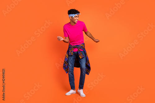 Full length body size photo of curious guy with headband dancing at party overjoyed isolated on vibrant orange color background