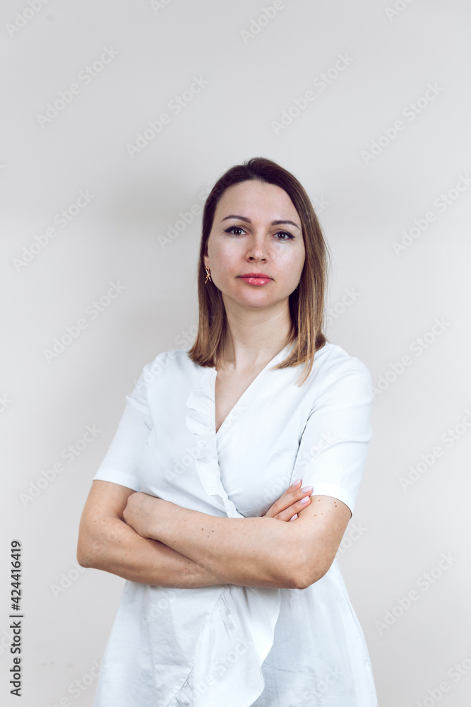 Beautiful young female doctor in a white medical gown, on an isolated white background. The beautician smiles into the camera, arms folded. With place for text or logo.