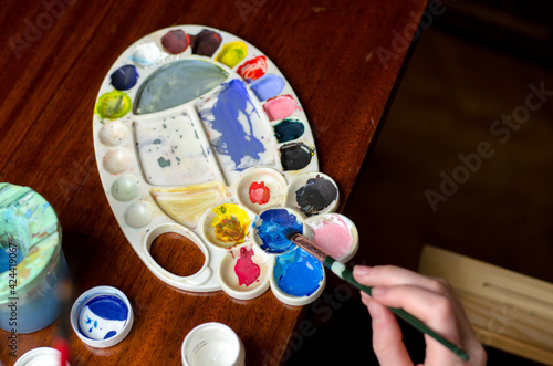 Children's hand holds a paintbrush. Artist dips a brush in blue paint