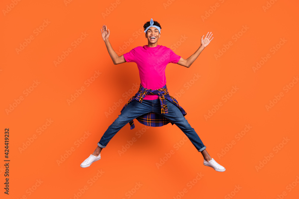 Full length body size photo of young hipster jumping up playful childish laughing isolated vibrant orange color background