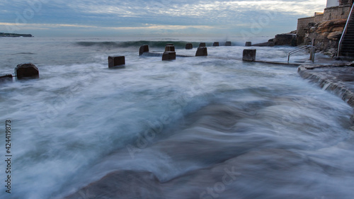 Wave coming over Coogee Beach coastline on cloudy morning.