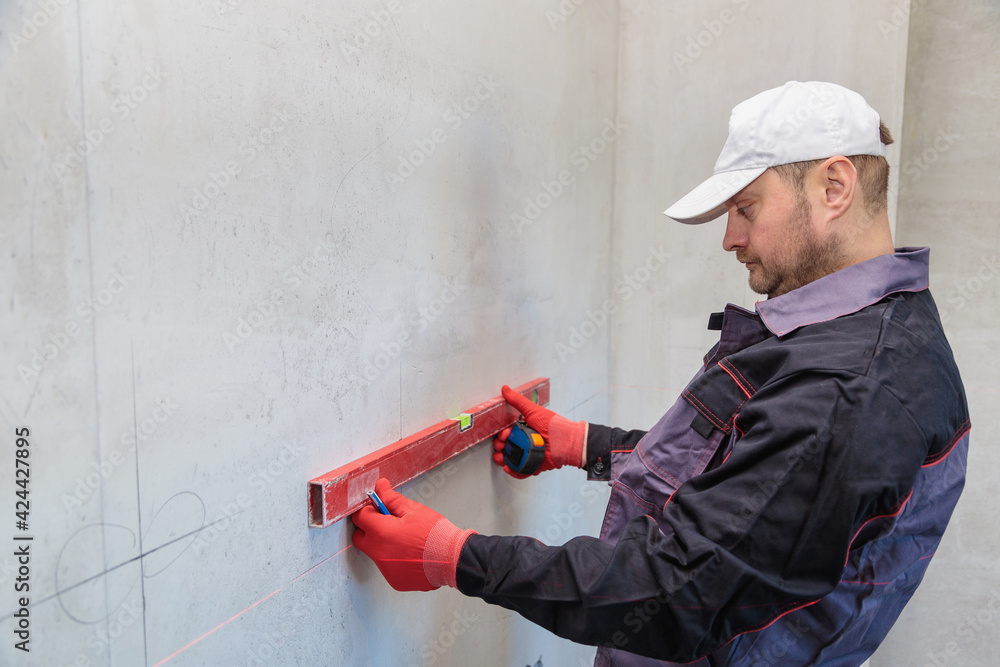 A man, an electrician marks out holes for sockets with a pencil, a tape measure A man, an electrician marks out holes for sockets with a pencil, a tape measure