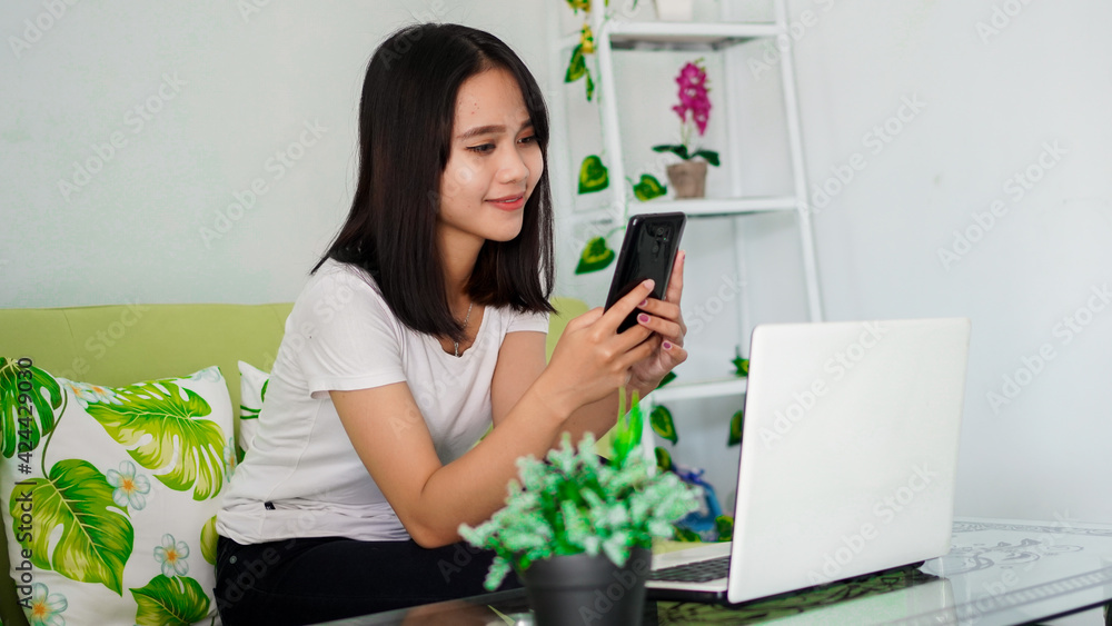 asian woman using mobile phone while working at home with laptop on chair asian woman using mobile phone while working at home with laptop on chair
