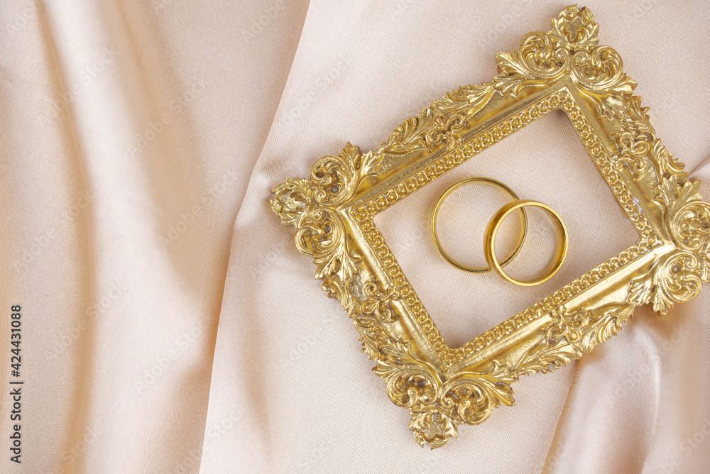 Two golden wedding rings close up with wooden picture frame on the cloth. Wedding invitation card concept. Two golden wedding rings close up with wooden picture frame on the cloth. Wedding invitation card concept.