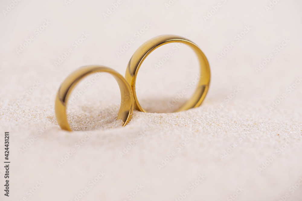 Two golden wedding rings close up on sand. Wedding on the beach invitation card concept. Two golden wedding rings close up on sand. Wedding on the beach invitation card concept.