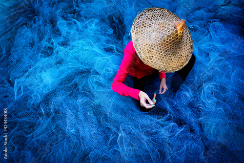 Women fisherman hands sewing blue fishing nets sitting on the ground and surrounded big net