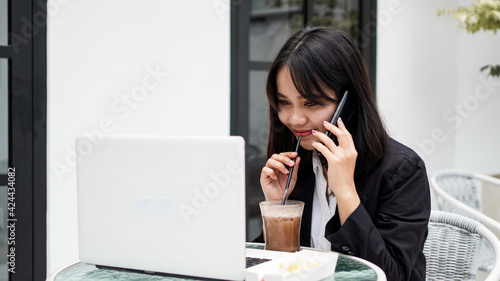 Asian business woman dringking coffe and talking on smartphone at cafe