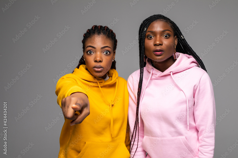 Two young african women are scared about something pointing fingers at camera isolated on gray background Two young african women are scared about something pointing fingers at camera isolated on gray background