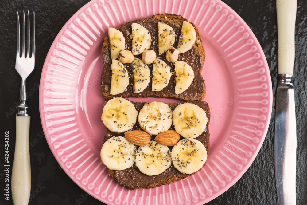 Toasted whole wheat bread with chocolate nuts paste nutella topping, banana, chia seeds, almonds and hazelnuts toast. Healthy proper nutrition for breakfast
