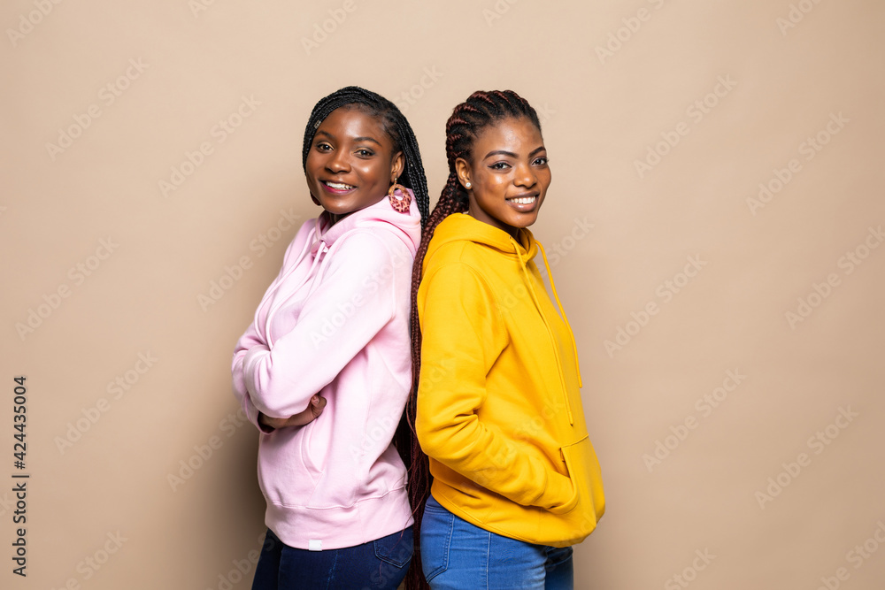 Portrait of two cheerful young women standing together isolated over beige background Portrait of two cheerful young women standing together isolated over beige background