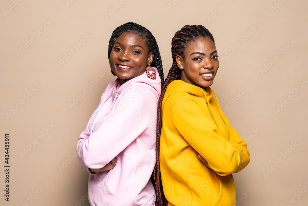 Portrait of two cheerful young women standing together isolated over beige background Portrait of two cheerful young women standing together isolated over beige background