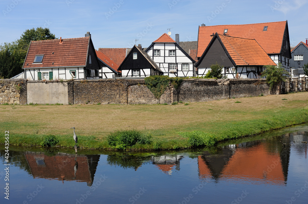 Heron in frong of picturesque half-timbered decorative houses in Westerholt village in Herten, North Rhine-Westphalia, Ruhr Area, Germany (Old Village Westerholt, Alte Freiheit Westerholt)