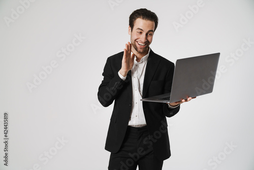 Unshaven brunette man in jacket gesturing while using laptop