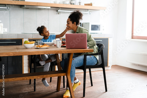 Happy mother and daughter having breakfast at table in home kitchen