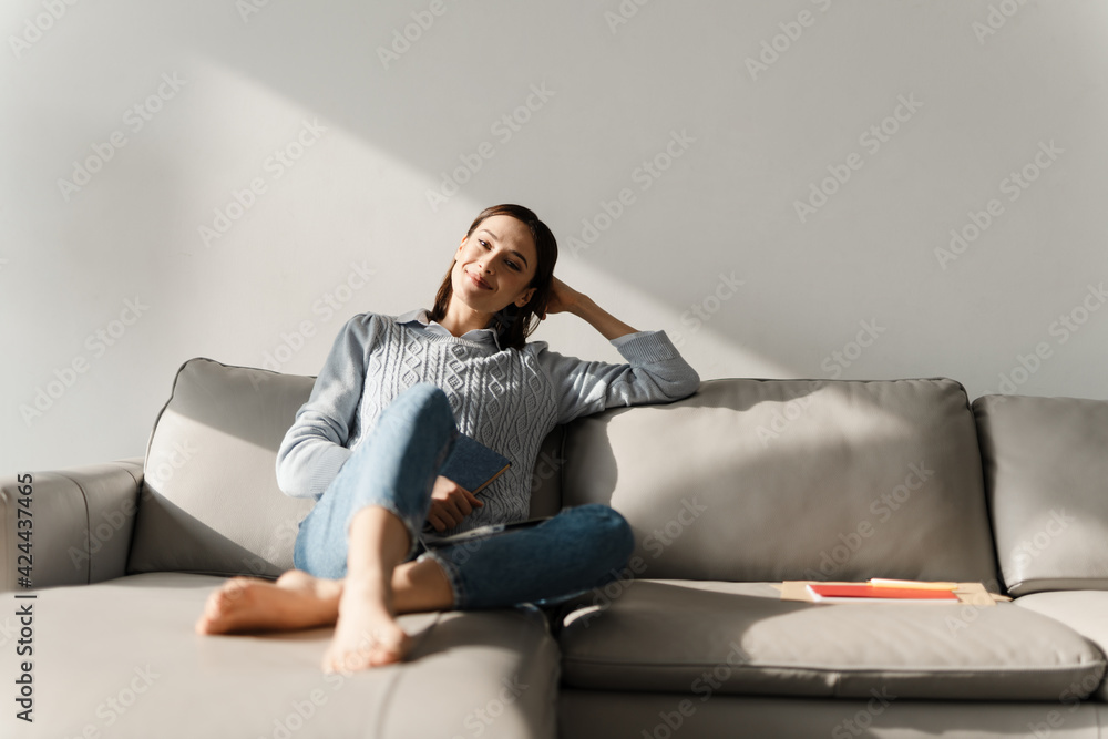 Young smiling woman holding planner while sitting on sofa at home