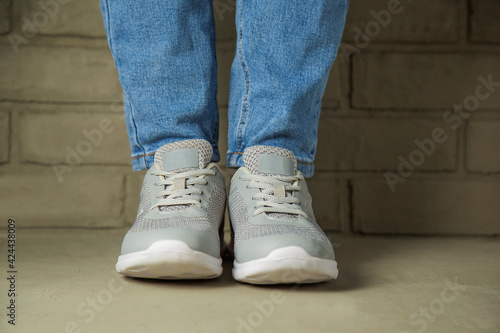 A woman in white sneakers stands against a brick wall in the background.