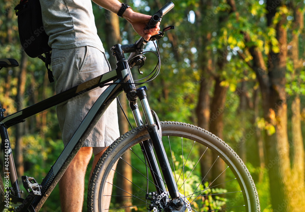 Close-up of a cyclist and a bicycle in a green sunny park. Summer time and the concept of an active lifestyle. Close-up of a cyclist and a bicycle in a green sunny park. Summer time and the concept of an active lifestyle.