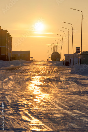 View of the street and buildings of a small arctic village at sunset. Bright golden sunlight. Winter arctic landscape. Daily life in the far north. Cold weather. Tavayvaam, Chukotka, Siberia, Russia. photo