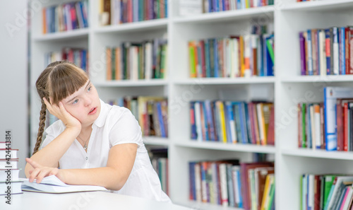 Pensive girl with syndrome down sits at library. Empty space for text. Education for disabled children concept