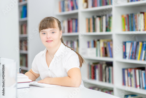 Portrait of a young girl with syndrome down at library. Empty space for text. Education for disabled children concept