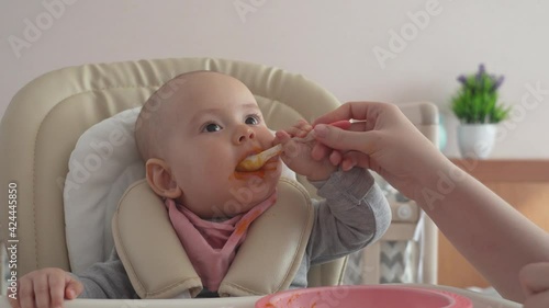 A newborn baby with a spoon tries to eat on its own. Feeding a newborn with pumpkin puree