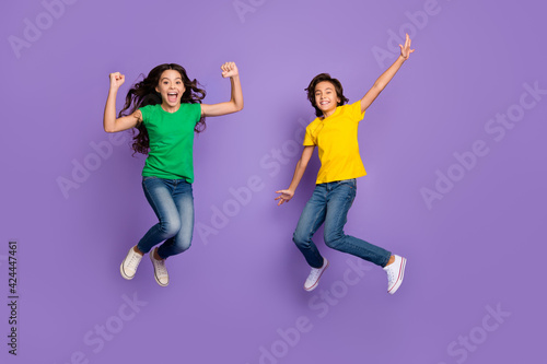 Full length photo of two excited kids happy smile celebrate win victory girl fists hands jump up isolated over purple color background