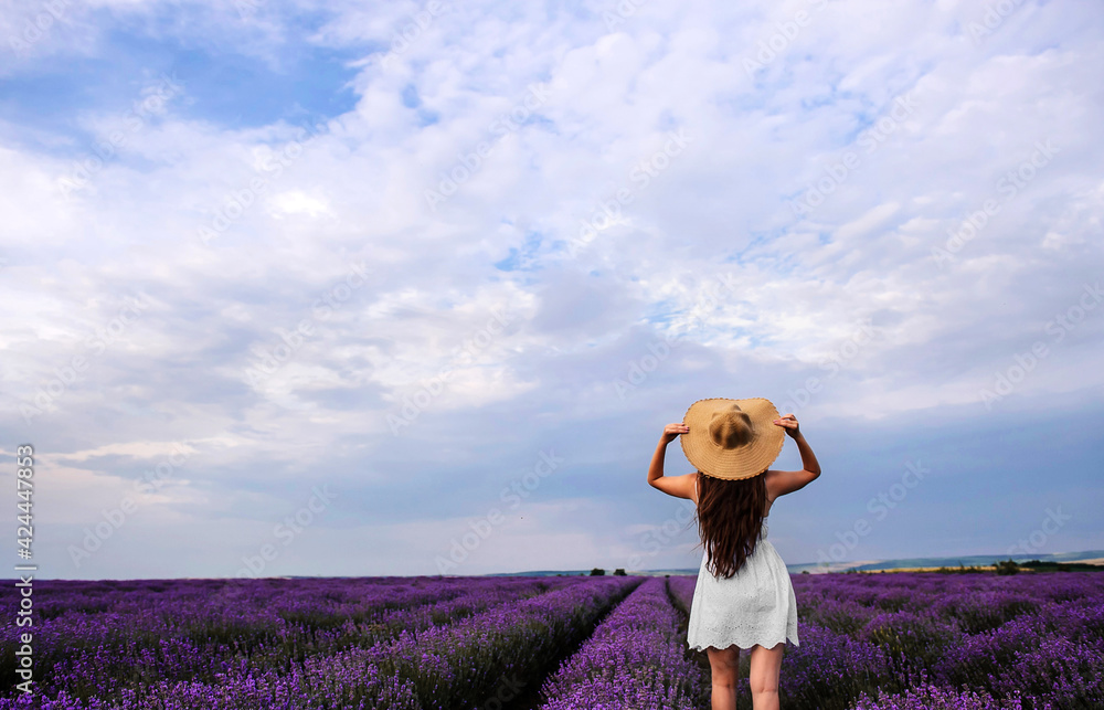 Back view of a young woman in white dress and straw hat walking in the lavender field. Back view of a young woman in white dress and straw hat walking in the lavender field.