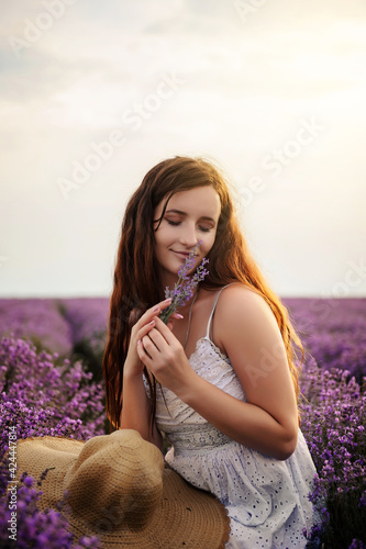 Portrait of a young woman in white dress and straw hat walking in the lavender field