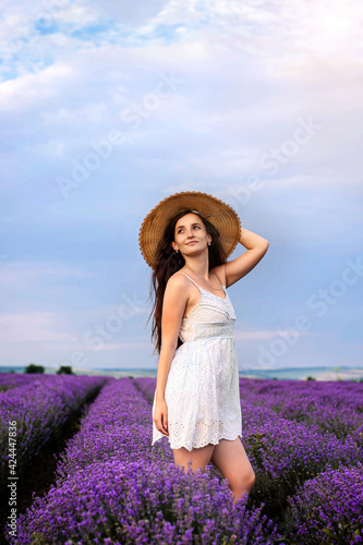 Fototapeta Naklejka Na Ścianę i Meble -  Portrait of a young woman in white dress and straw hat walking in the lavender field