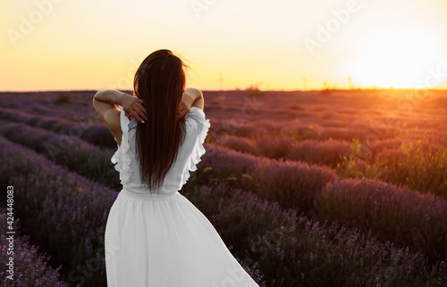 Back view of a young woman in white dress walking in the lavender field.