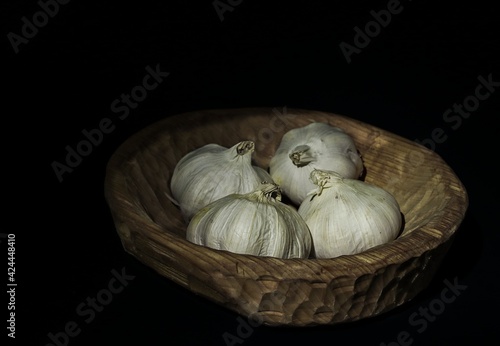 Garlic in wooden bowl and on black background