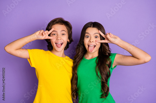 Photo of two little boy and girl make funny face tongue out show v-sign isolated on purple color background